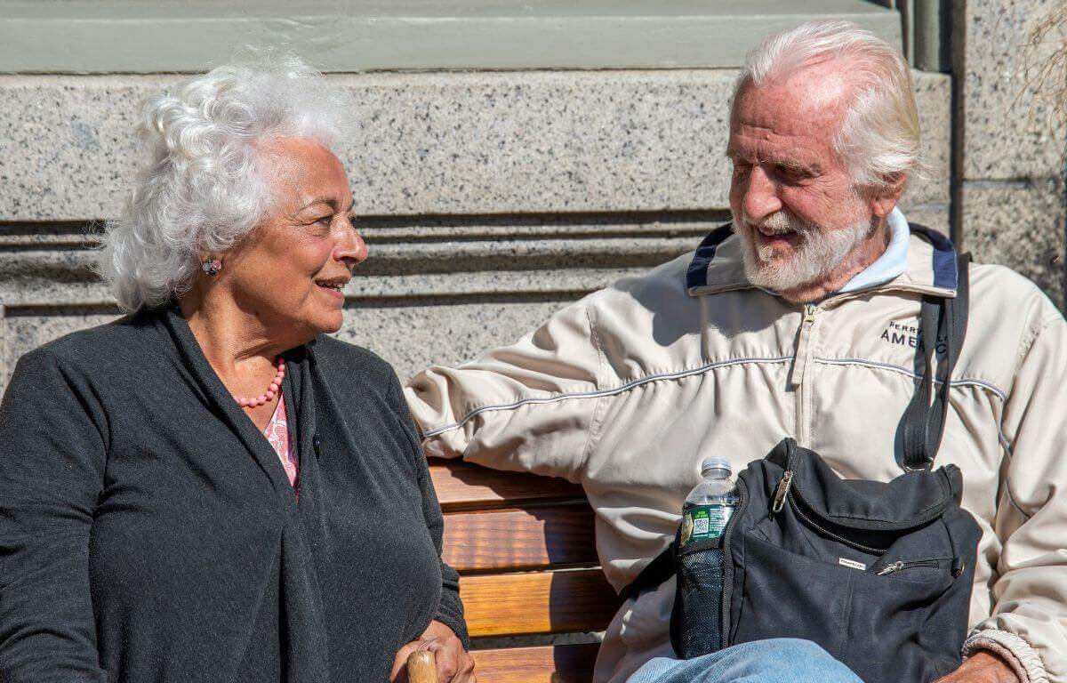 Un couple de retraités souriants et sereins sur un banc au soleil, image de la retraite qu'on prépare à 30 ans avec un petit salaire