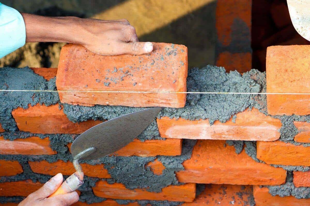 Un maçon pose brique après brique, comme pour construire son patrimoine avec un petit salaire