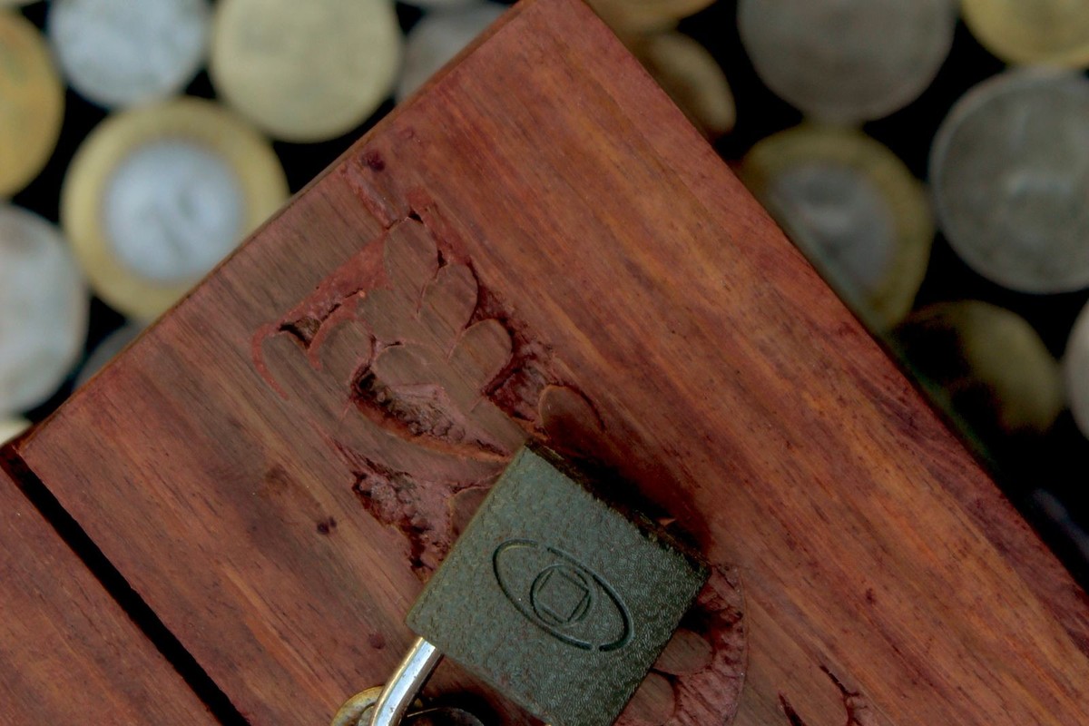 Coffret en bois cadenassé sur un lit de pièces, symbole de l'épargne bloquée du PER face à l'assurance-vie.