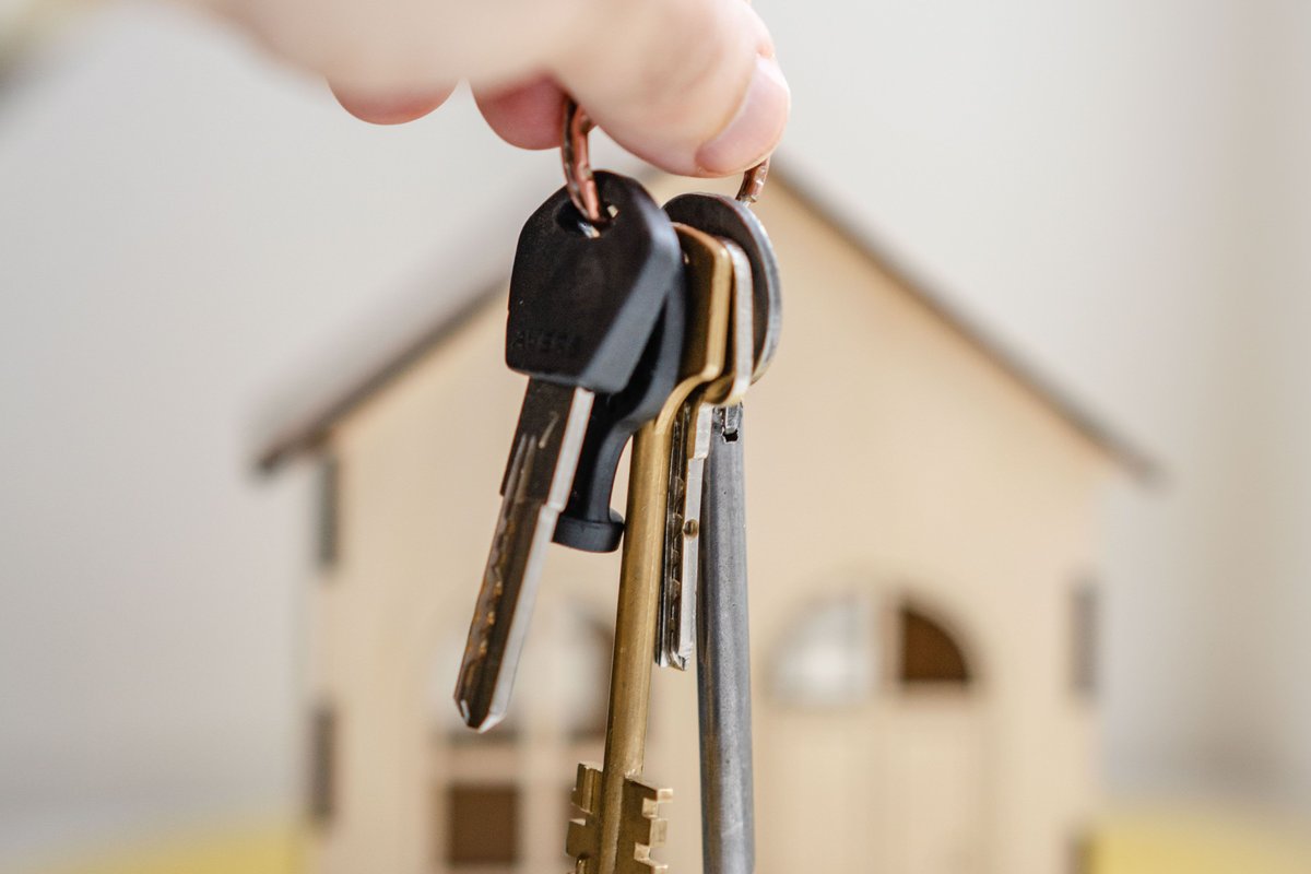 Main tenant un trousseau de clés au-dessus d'une maison miniature pour devenir propriétaire avec un petit salaire